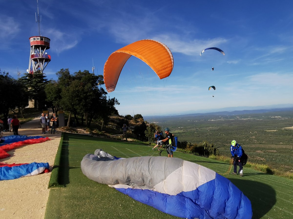 Photo d'une aire d'envol de parapentes, avec plusieurs personnes qui décollent ou s'apprêtent à le faire